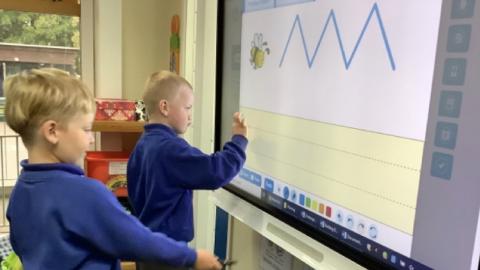 two children practising their handwriting on an interactive whiteboard