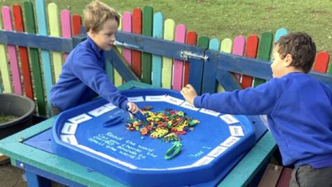 two boys picking up letter sounds with tweezers outside