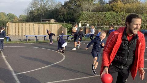 children and a man in a red coat running around the playground