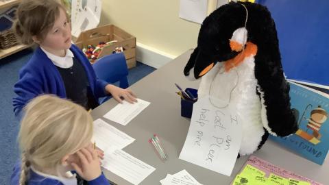 Children writing about a cuddly toy penguin