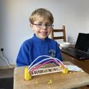 A boy standing next to his bridge made out of play dough, art straws and pipe cleaners 