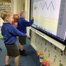 two children practising their handwriting on an interactive whiteboard