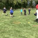 Children running with a ball on the field with their PE teacher